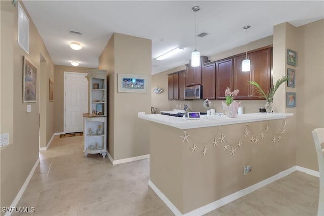 kitchen featuring stainless steel microwave, decorative light fixtures, baseboards, and a peninsula