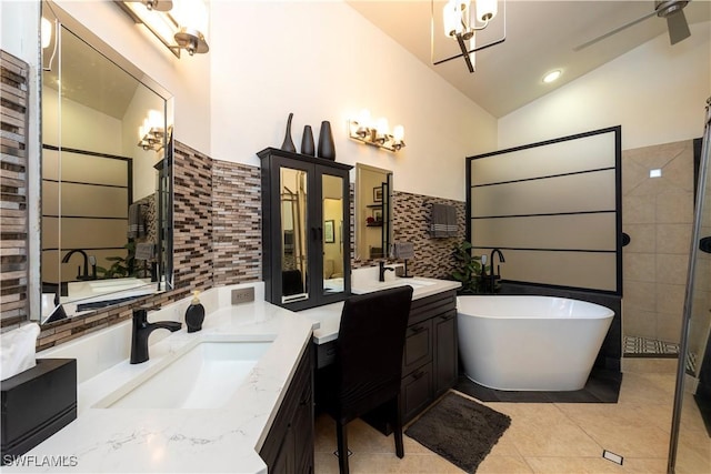 full bath featuring tiled shower, a freestanding bath, two vanities, a sink, and vaulted ceiling