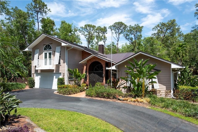 view of front of house featuring an attached garage, a chimney, stairs, and aphalt driveway