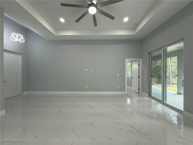 spare room with baseboards, ceiling fan, a tray ceiling, and marble finish floor