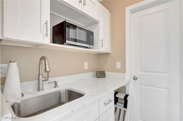 kitchen featuring white cabinetry, light stone counters, and a sink