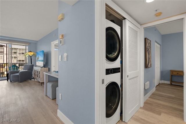 laundry room with laundry area, baseboards, stacked washer / drying machine, and light wood-type flooring