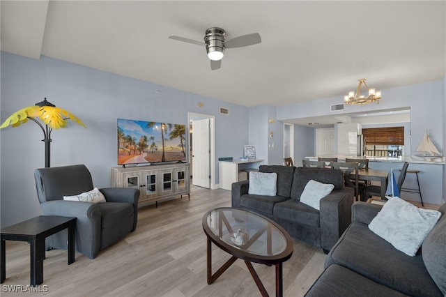 living area with ceiling fan with notable chandelier, light wood-type flooring, and visible vents