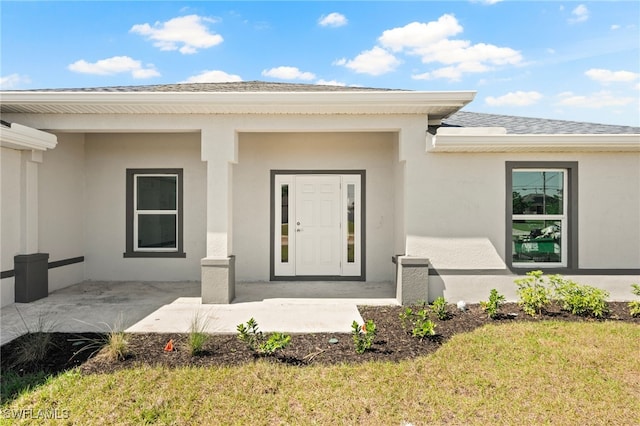 entrance to property featuring stucco siding, a yard, and roof with shingles