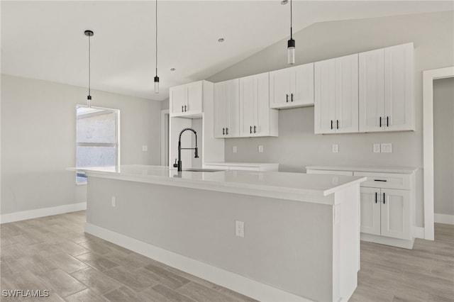 kitchen featuring white cabinets, a sink, baseboards, vaulted ceiling, and a kitchen island with sink