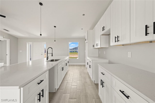 kitchen with a sink, light wood-style floors, white cabinetry, pendant lighting, and an island with sink