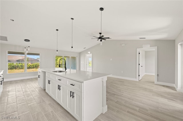 kitchen featuring white cabinetry, light wood-style floors, ceiling fan, a sink, and baseboards