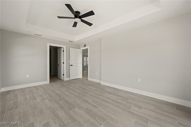 unfurnished bedroom with ceiling fan, a raised ceiling, visible vents, baseboards, and a spacious closet