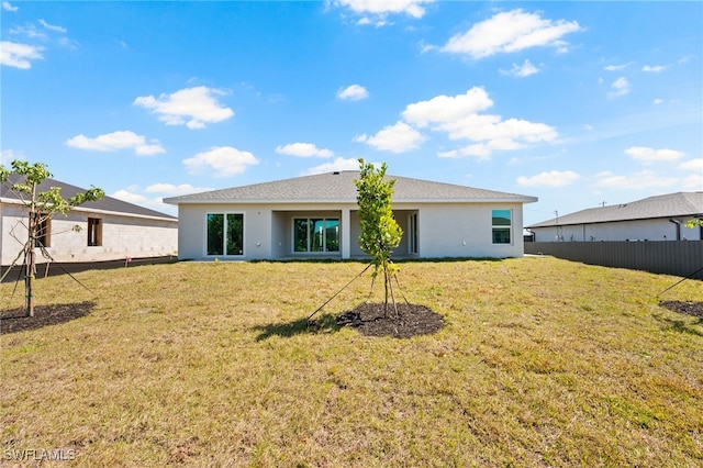 rear view of house featuring fence, stucco siding, and a yard