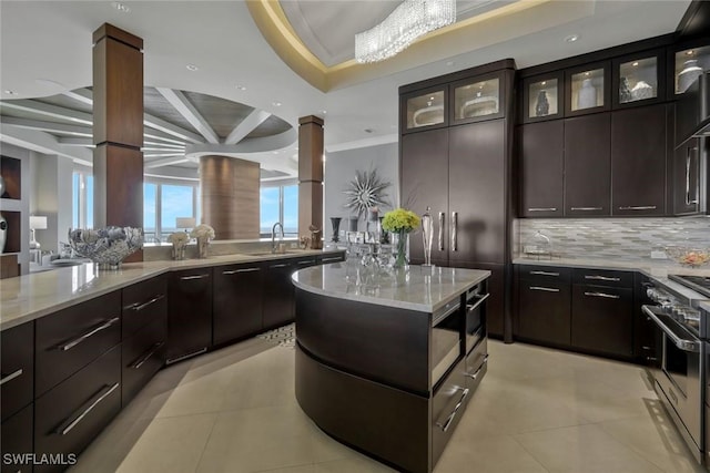 kitchen featuring high end stainless steel range oven, a sink, decorative backsplash, glass insert cabinets, and light stone countertops