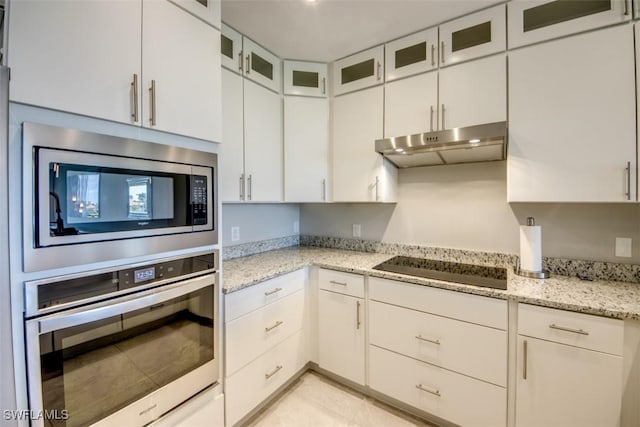 kitchen featuring glass insert cabinets, under cabinet range hood, light stone counters, and appliances with stainless steel finishes