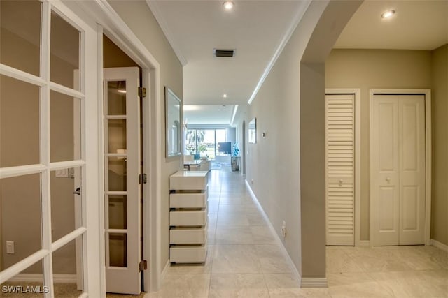 corridor with arched walkways, visible vents, baseboards, and light tile patterned floors