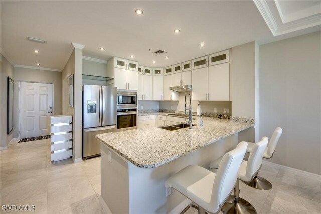 kitchen featuring a peninsula, glass insert cabinets, appliances with stainless steel finishes, light stone countertops, and ornamental molding