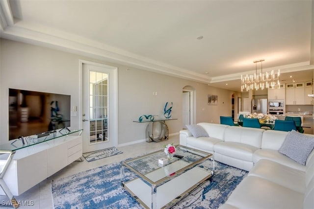 living room with a tray ceiling, arched walkways, and an inviting chandelier