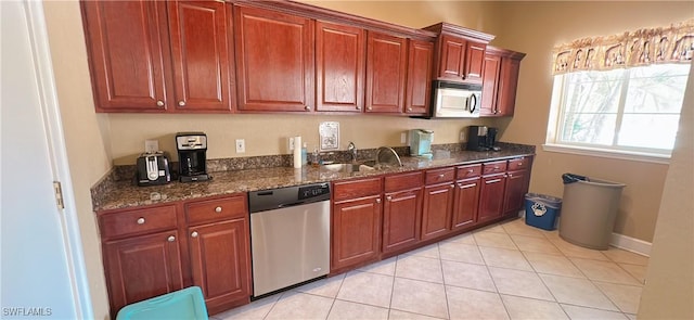kitchen with dark stone counters, stainless steel appliances, light tile patterned floors, and a sink