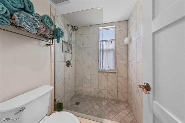 bathroom with tiled shower, visible vents, and toilet