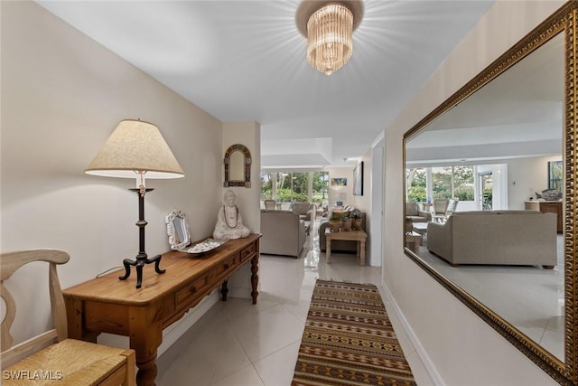 hall featuring baseboards, tile patterned flooring, a notable chandelier, and a healthy amount of sunlight