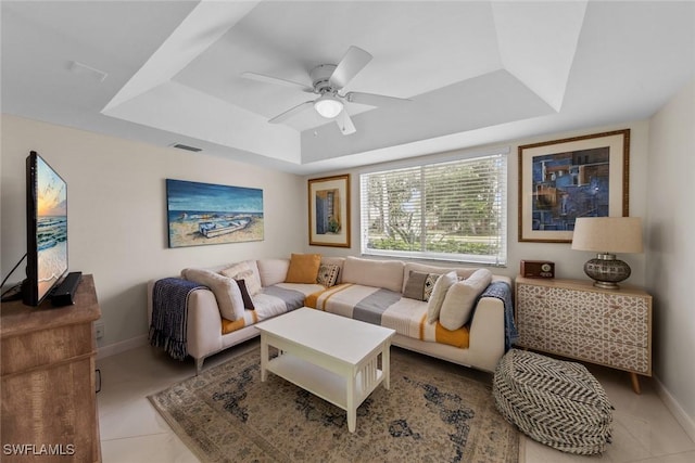 living room featuring light tile patterned floors, ceiling fan, a raised ceiling, baseboards, and visible vents