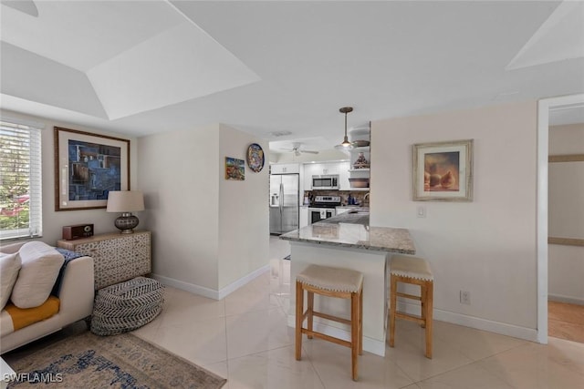 interior space with a kitchen breakfast bar, a ceiling fan, light stone countertops, a peninsula, and appliances with stainless steel finishes