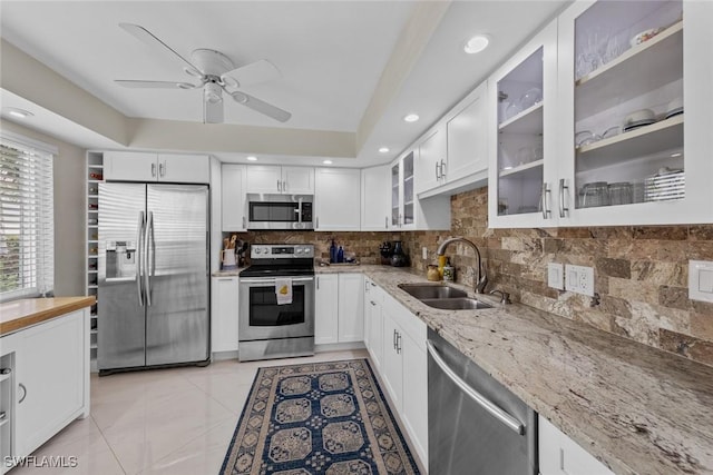 kitchen featuring light stone counters, a sink, decorative backsplash, ceiling fan, and stainless steel appliances