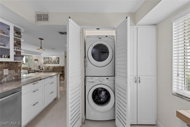 laundry area featuring light tile patterned floors, visible vents, stacked washer / dryer, and laundry area