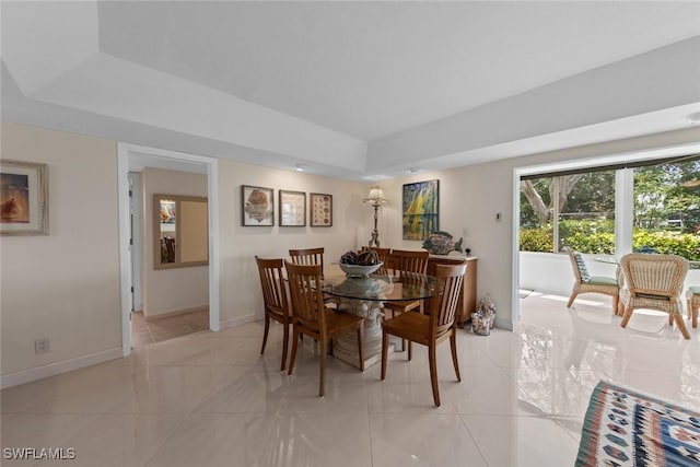 dining space with baseboards, a tray ceiling, and light tile patterned floors
