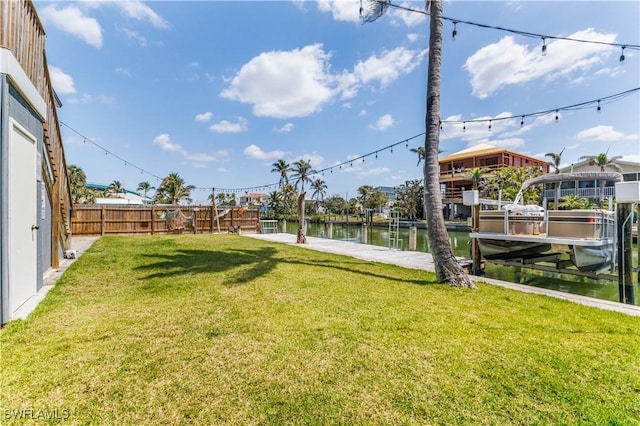 view of yard featuring boat lift, fence, a boat dock, and a water view