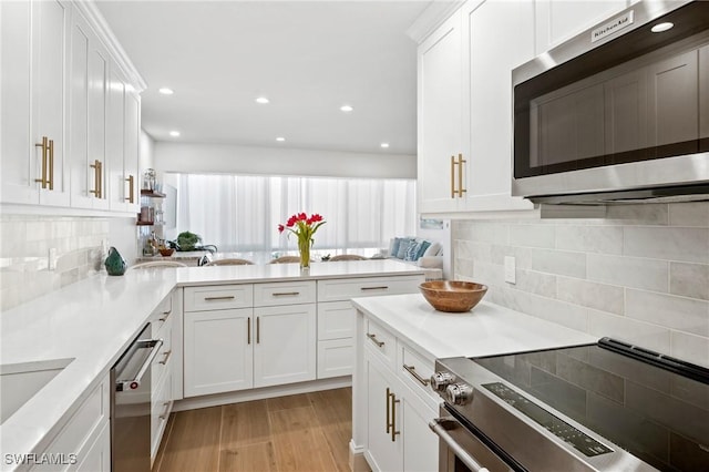 2100 Gulf Shore Blvd N Unit 108, Naples, FL 34102 - kitchen with stainless steel appliances, light wood finished floors, white cabinets, a peninsula, and light countertops