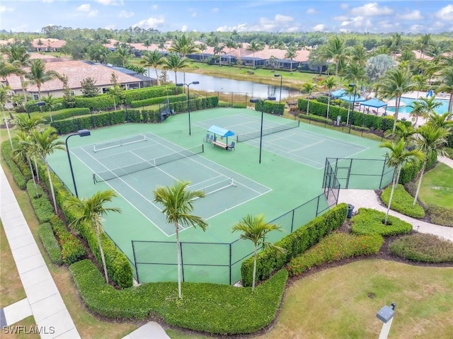view of tennis court featuring fence, a residential view, and a water view
