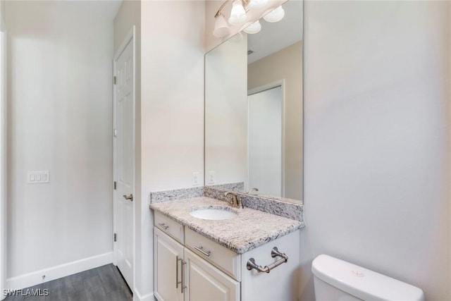 bathroom featuring baseboards, wood finished floors, toilet, and vanity