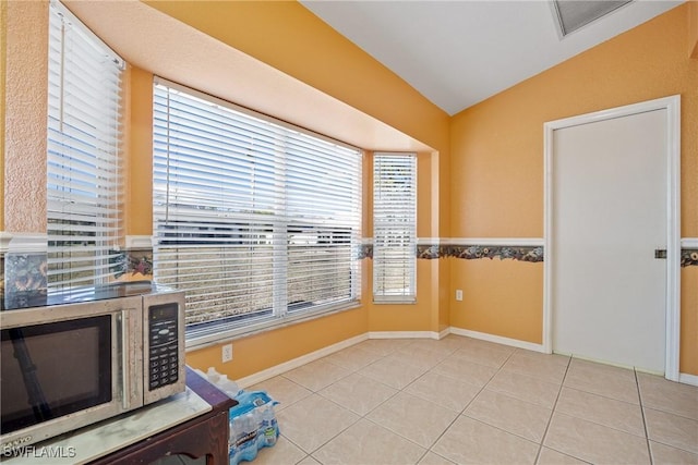 interior space with lofted ceiling, light tile patterned floors, stainless steel microwave, and baseboards