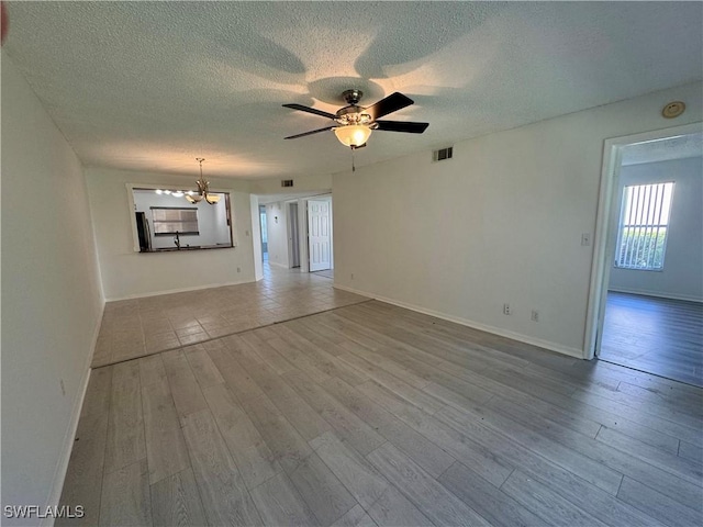 unfurnished living room featuring visible vents, baseboards, a textured ceiling, wood finished floors, and ceiling fan with notable chandelier