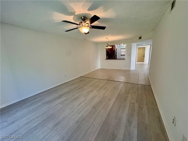 empty room featuring a textured ceiling, light wood-style flooring, visible vents, baseboards, and ceiling fan with notable chandelier