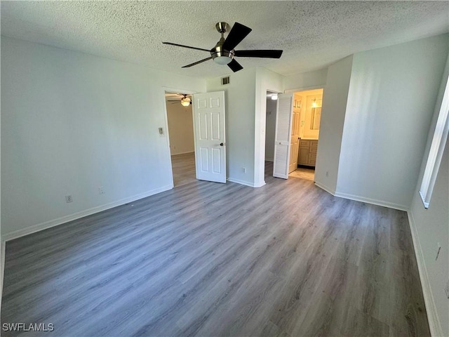 unfurnished bedroom with a textured ceiling, wood finished floors, a walk in closet, and baseboards