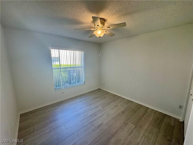 empty room with a textured ceiling, ceiling fan, wood finished floors, and baseboards
