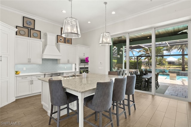 kitchen featuring an island with sink, stainless steel appliances, backsplash, a sink, and white cabinetry