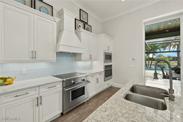 6348 Lyford Isle Dr, Naples, FL 34113 - kitchen with stainless steel appliances, a sink, crown molding, custom range hood, and white cabinetry