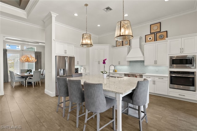 6348 Lyford Isle Dr, Naples, FL 34113 - kitchen with appliances with stainless steel finishes, custom exhaust hood, a sink, ornamental molding, and a kitchen bar