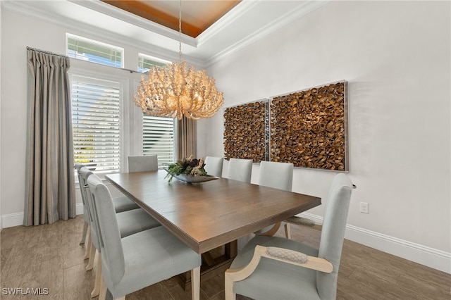 dining space with a tray ceiling, light wood-type flooring, baseboards, a notable chandelier, and crown molding
