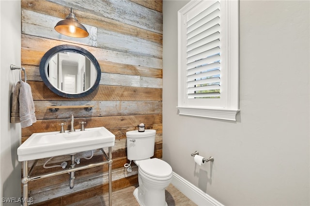 bathroom with wood walls, toilet, a sink, and baseboards