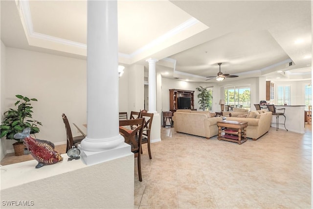 living area with light tile patterned floors, ornamental molding, ornate columns, a raised ceiling, and a ceiling fan
