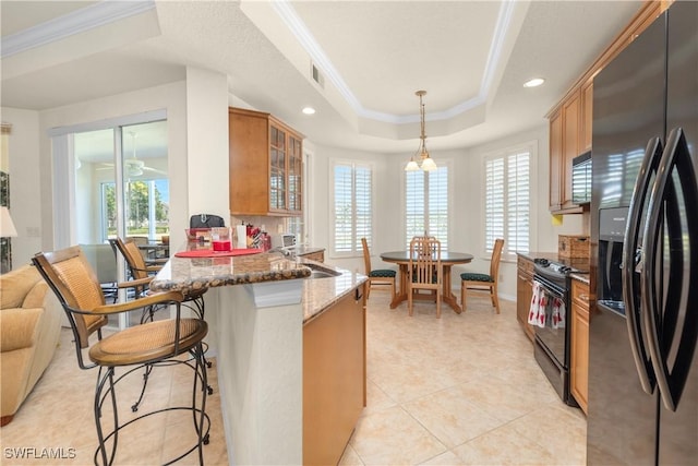 kitchen with glass insert cabinets, dark stone countertops, a tray ceiling, black appliances, and ornamental molding