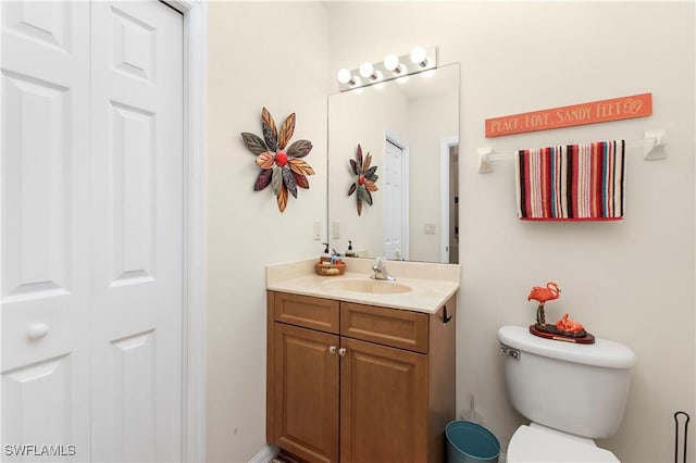 bathroom with toilet, vanity, and a closet