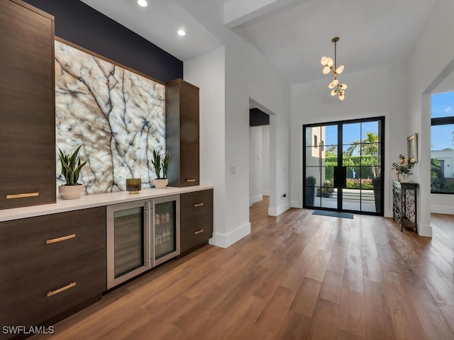 bar featuring a high ceiling, an inviting chandelier, wood finished floors, pendant lighting, and baseboards