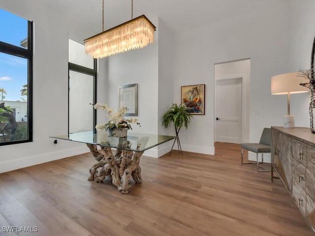 dining area with baseboards, wood finished floors, a towering ceiling, and a notable chandelier