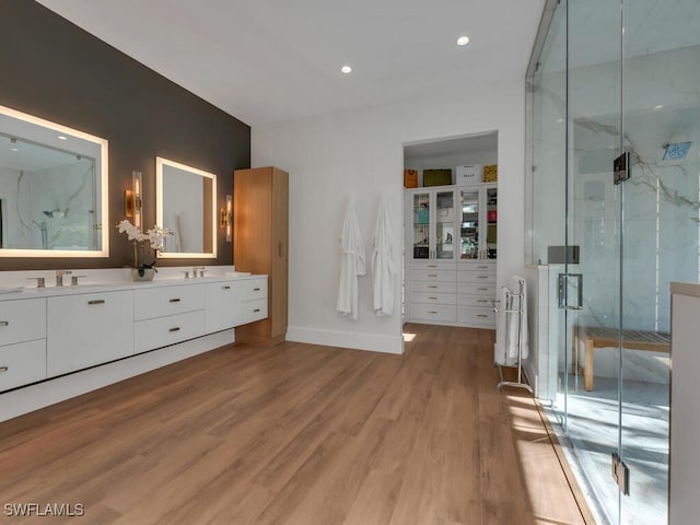 bathroom featuring a marble finish shower, double vanity, baseboards, recessed lighting, and wood finished floors