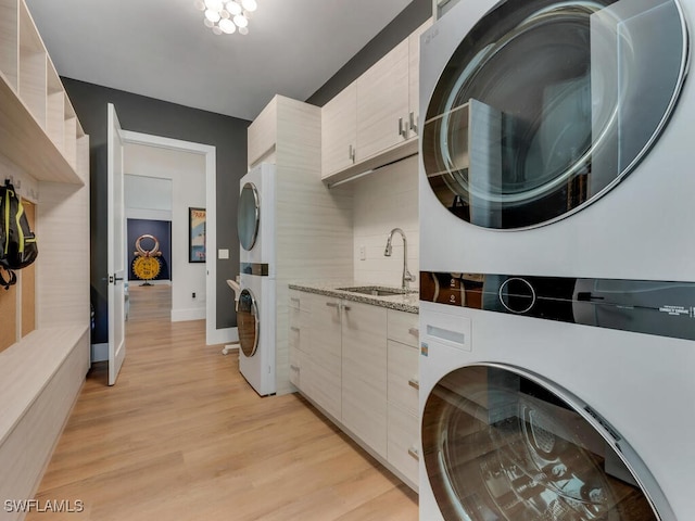 clothes washing area featuring cabinet space, light wood-type flooring, stacked washer / dryer, and a sink