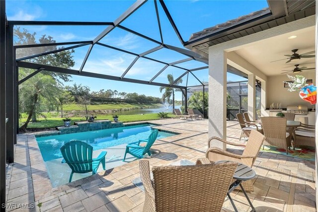 outdoor pool featuring exterior kitchen, ceiling fan, a water view, a patio area, and glass enclosure