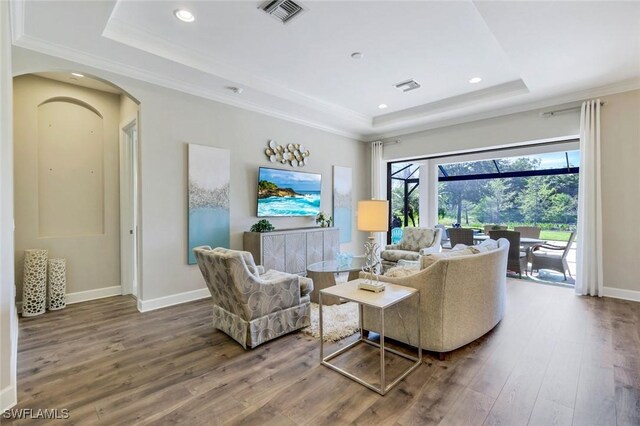 living room with visible vents, ornamental molding, a raised ceiling, and hardwood / wood-style floors