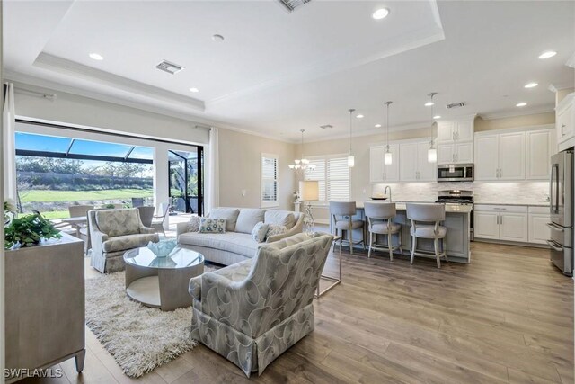living area featuring visible vents, ornamental molding, light wood finished floors, and a raised ceiling